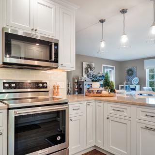 Modern kitchen with stainless appliances, white cabinets, and pendant lighting.