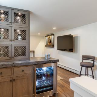 Basement wet bar with shelves, TV, and seating area featuring wood finishes.