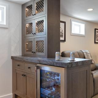 Modern kitchen bar with wine fridge, storage cabinets, and drinks on the counter.