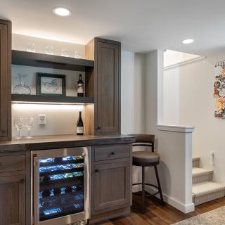 Modern home bar with wine fridge, glasses, and art, next to a staircase.