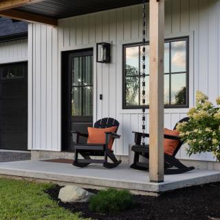 Modern home entrance with rocking chairs and a flowering bush on the porch.