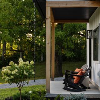 Comfortable rocking chairs on a porch surrounded by greenery and flowering shrubs.