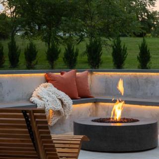 Cozy outdoor seating area with a fire pit, orange cushions, and a knitted blanket.