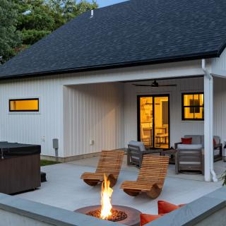 Modern backyard with a fire pit, lounge chairs, and a view of a white house at dusk.