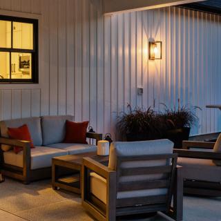 Cozy outdoor seating area with warm lighting and a grill in the background.