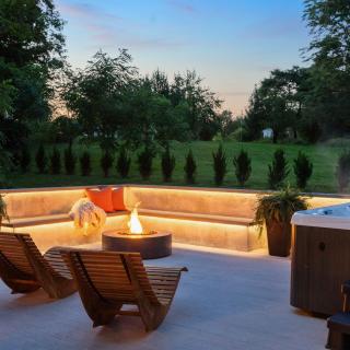 Cozy outdoor seating area with a fire pit and hot tub, surrounded by greenery.