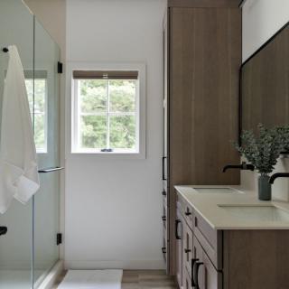 Modern bathroom featuring a glass shower, wooden cabinetry, and a window for natural light.