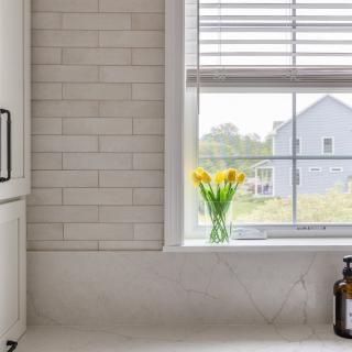 Bright kitchen window with yellow tulips and a marble counter, featuring a hand soap dispenser.