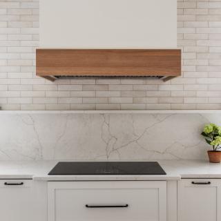 Modern kitchen with white cabinets, marble countertop, and wooden range hood.