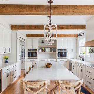 Bright, modern kitchen with a large island, white cabinetry, and wooden beams.