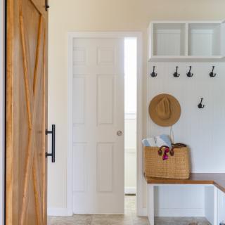 Bright entryway with a sliding wooden door, hooks, a basket, and shoes on the floor.