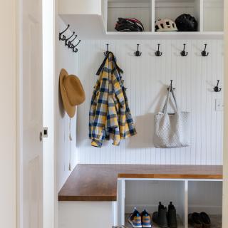 Bright entryway with a bench, hooks, hats, coats, and various footwear.