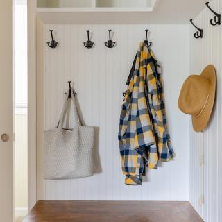 Mudroom with hooks, a plaid coat, a bag, and a straw hat on a wooden bench.