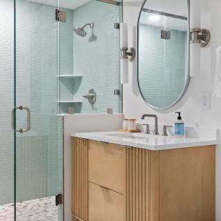 Modern bathroom with glass shower, wood vanity, and circular mirror.