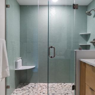 Modern glass shower with textured green walls and pebble-stone floor.