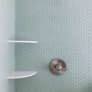 Shower stall with a silver showerhead, green tiled wall, and white shelves.