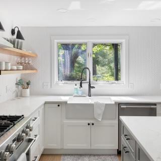 Bright modern kitchen with white cabinets, a farmhouse sink, and wooden shelves.