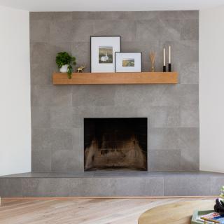 Modern living room with a gray stone fireplace, wood shelf, and artwork.