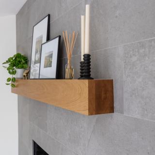 Wooden shelf on a gray wall with photos, a plant, and decorative items.