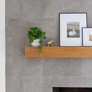 Wooden shelf with potted plant, decorative elephant, and framed photos on a gray stone wall.